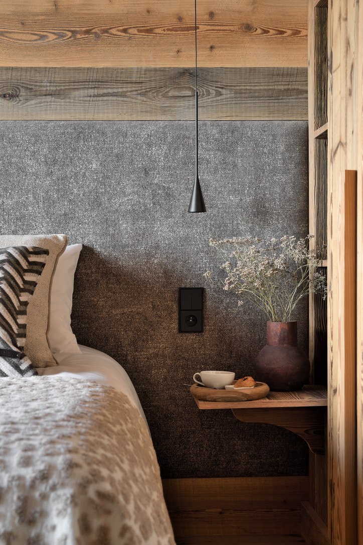 Détail de chambre au 2e étage : tête de lit en tissu gris, lampe suspendue noire et vase de fleurs séchées