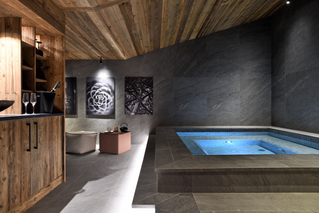 Vue d'ensemble du spa Arcabulle : jacuzzi en pierre, œuvres murales et charpente de bois ancien