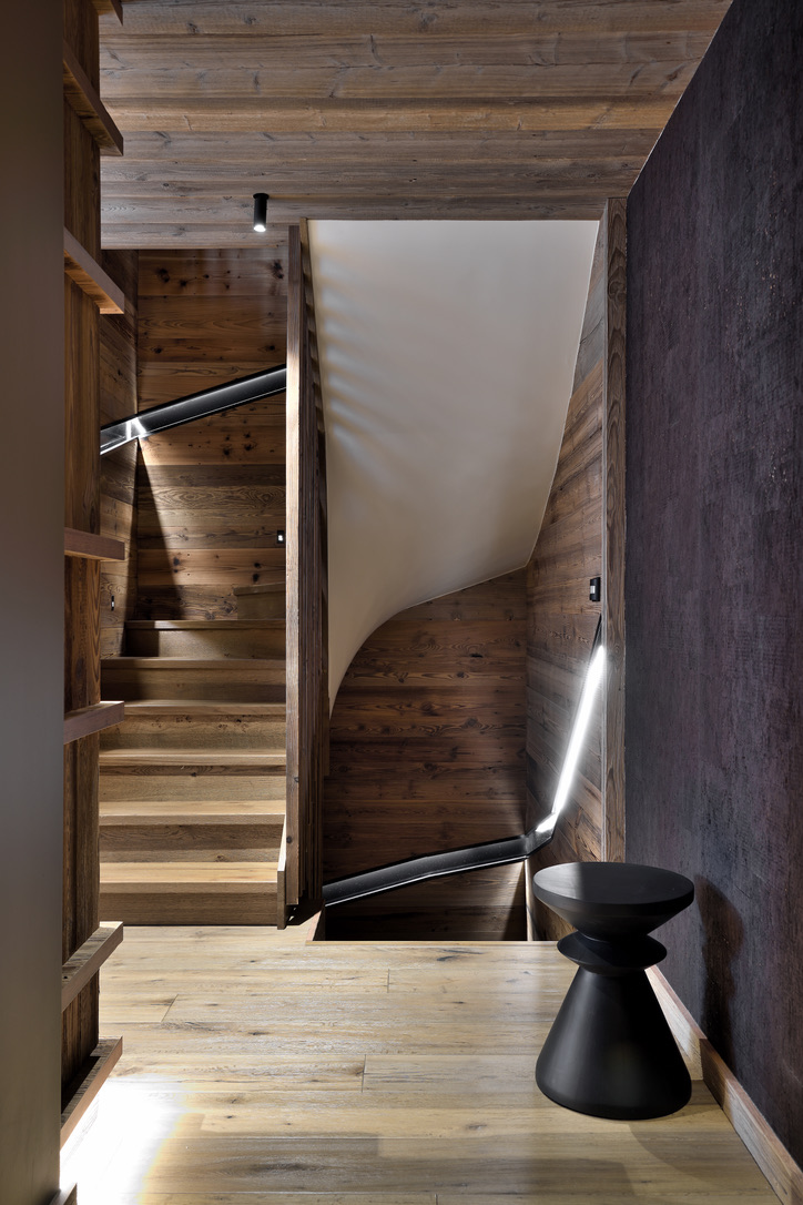 Escalier de bois reliant les niveaux du chalet, rampe éclairée et tabouret sculptural