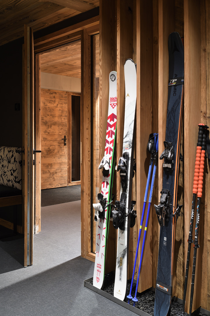 Entrée du ski-room d'Epicime Lodge : skis et bâtons rangés contre les panneaux de vieux bois