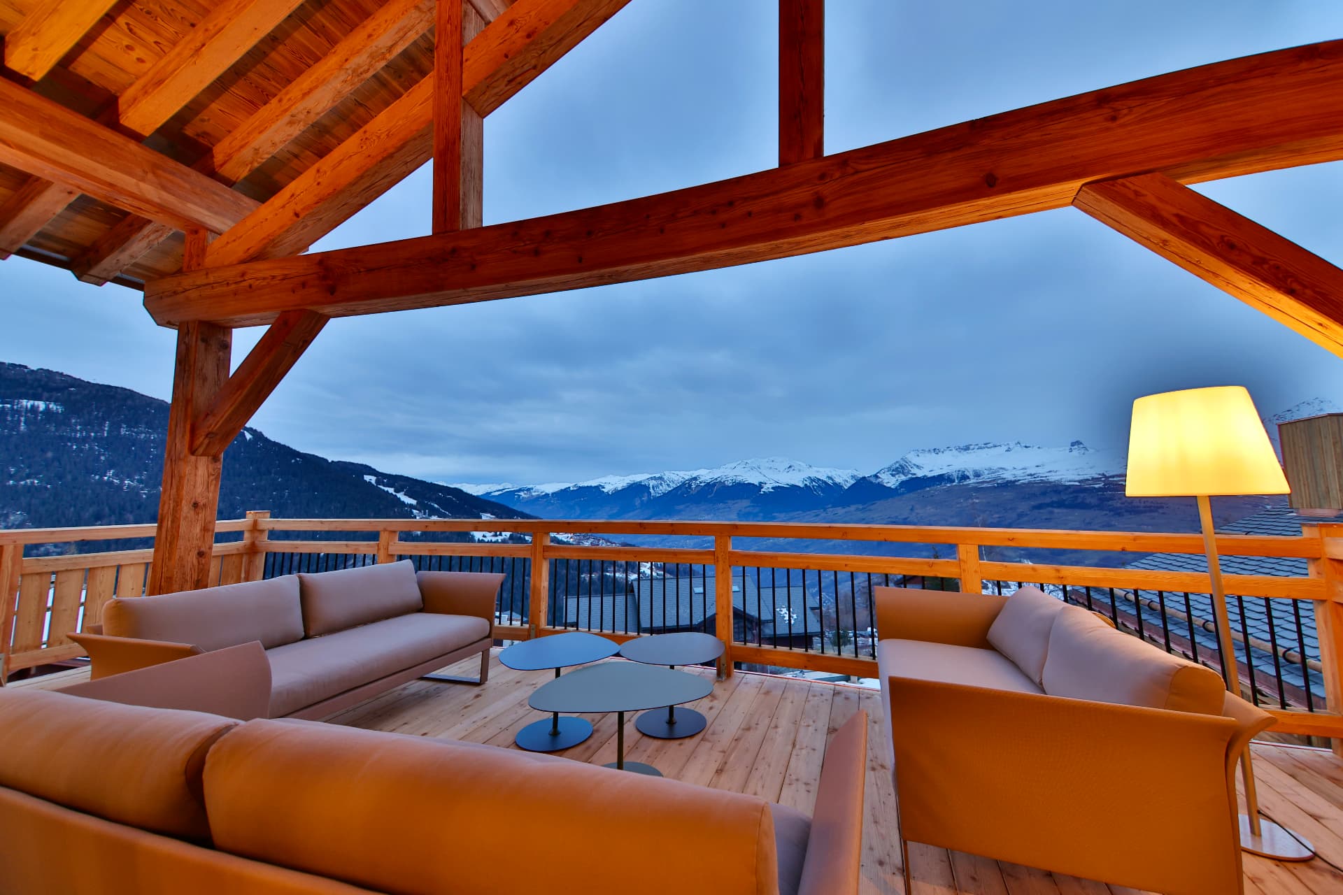 Terrasse couverte d'Epicime Lodge au crépuscule, canapés face aux sommets enneigés de Paradiski